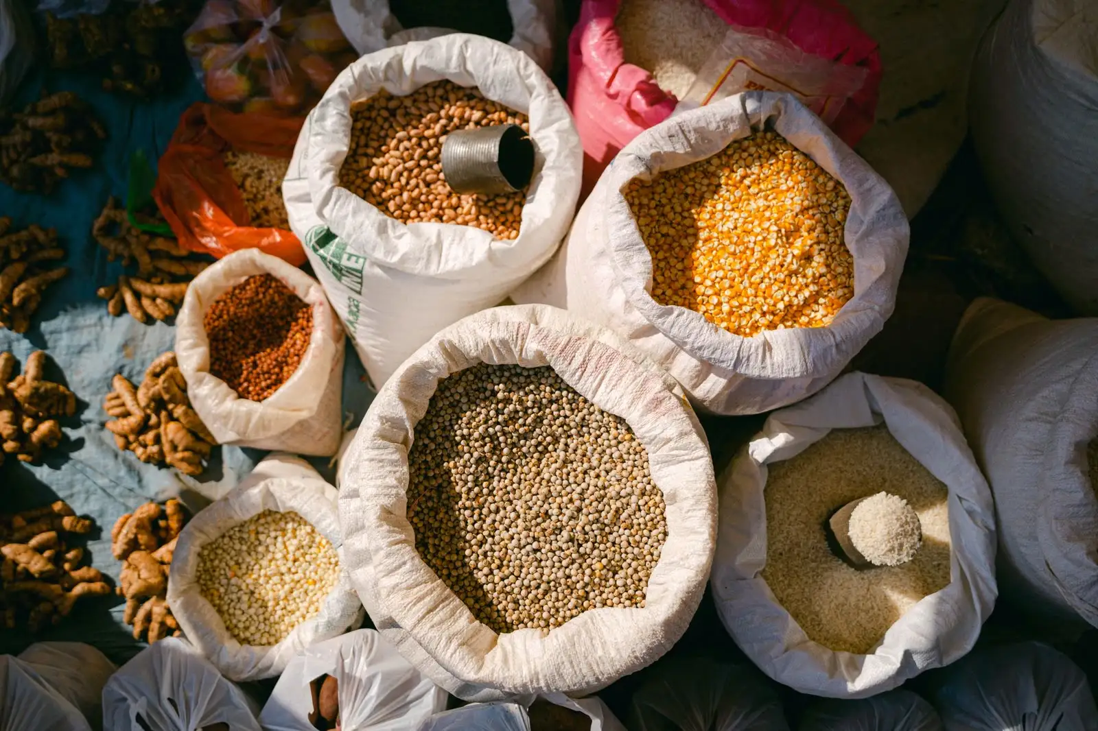 Open white PP woven sacks of beans, corn, and rice seen from above at a market
